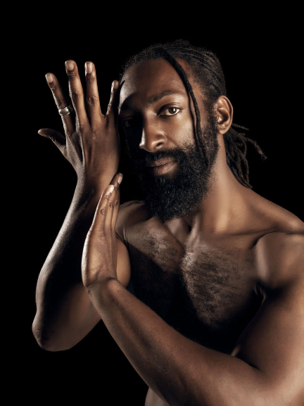 Purple Fire Crow, also known as Antoine Hunter, is bare chested, his hands gesturing toward his face. He is an award-winning African, Indigenous, Deaf, Disabled, Two Spirit producer, choreographer, film/theater actor, dancer, speaker, mentor, and Deaf advocate. He is founder of Bay Area International Deaf Dance Festival, Urban Jazz Dance Company, and #DeafWoke talk show.