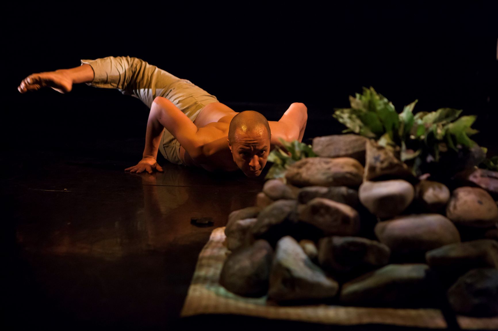 Bare-chested man on stomach gazes at tower of stones
