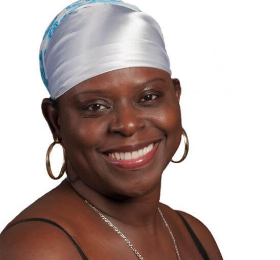 Woman with gold hoop earrings and a white satin head scarf smiles