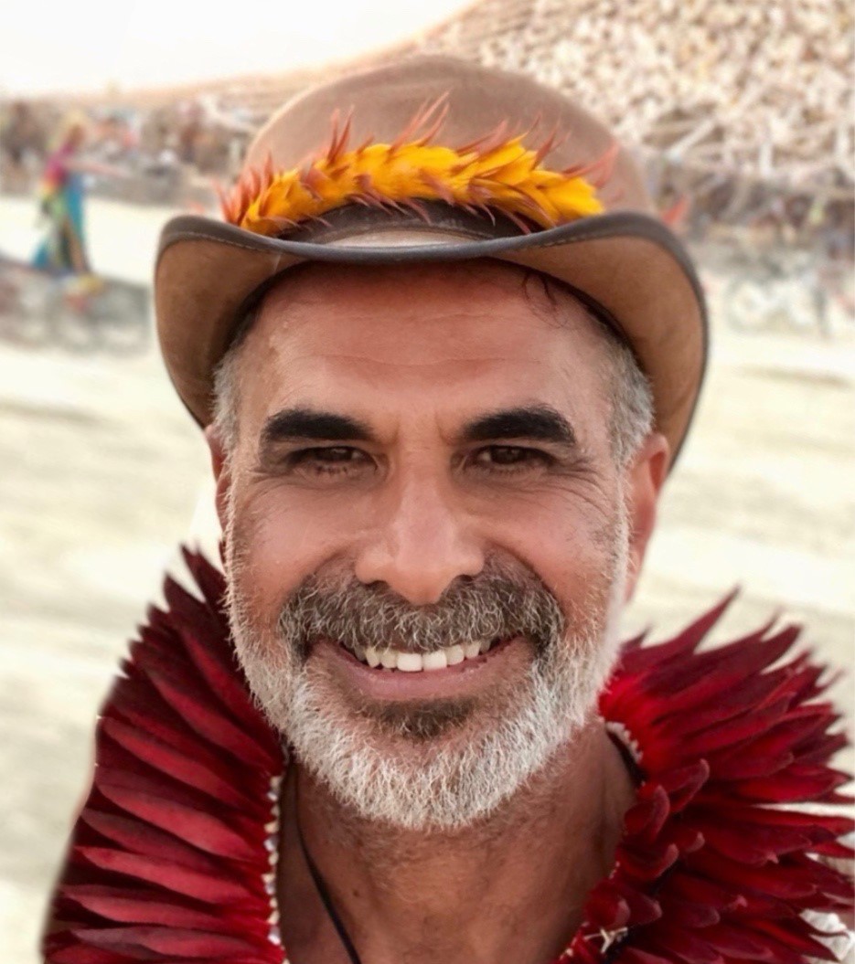 Makuakane poses wearing a brown hat and auburn feather necklace around his neck