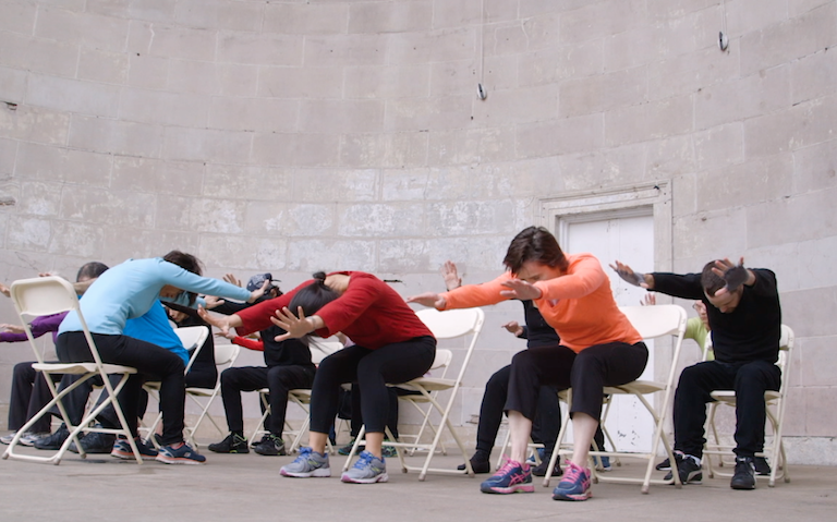 Dancers in chairs bent over with arms outstretched