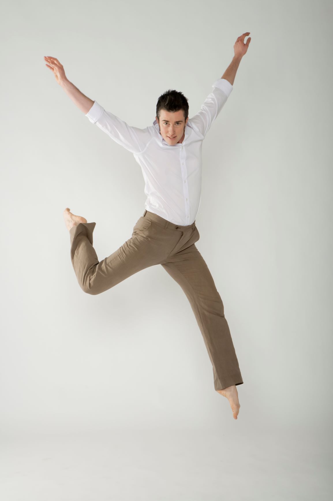 Dorsey in white shirt and tan pants, jumping in the air, back knee bent, both arms raised