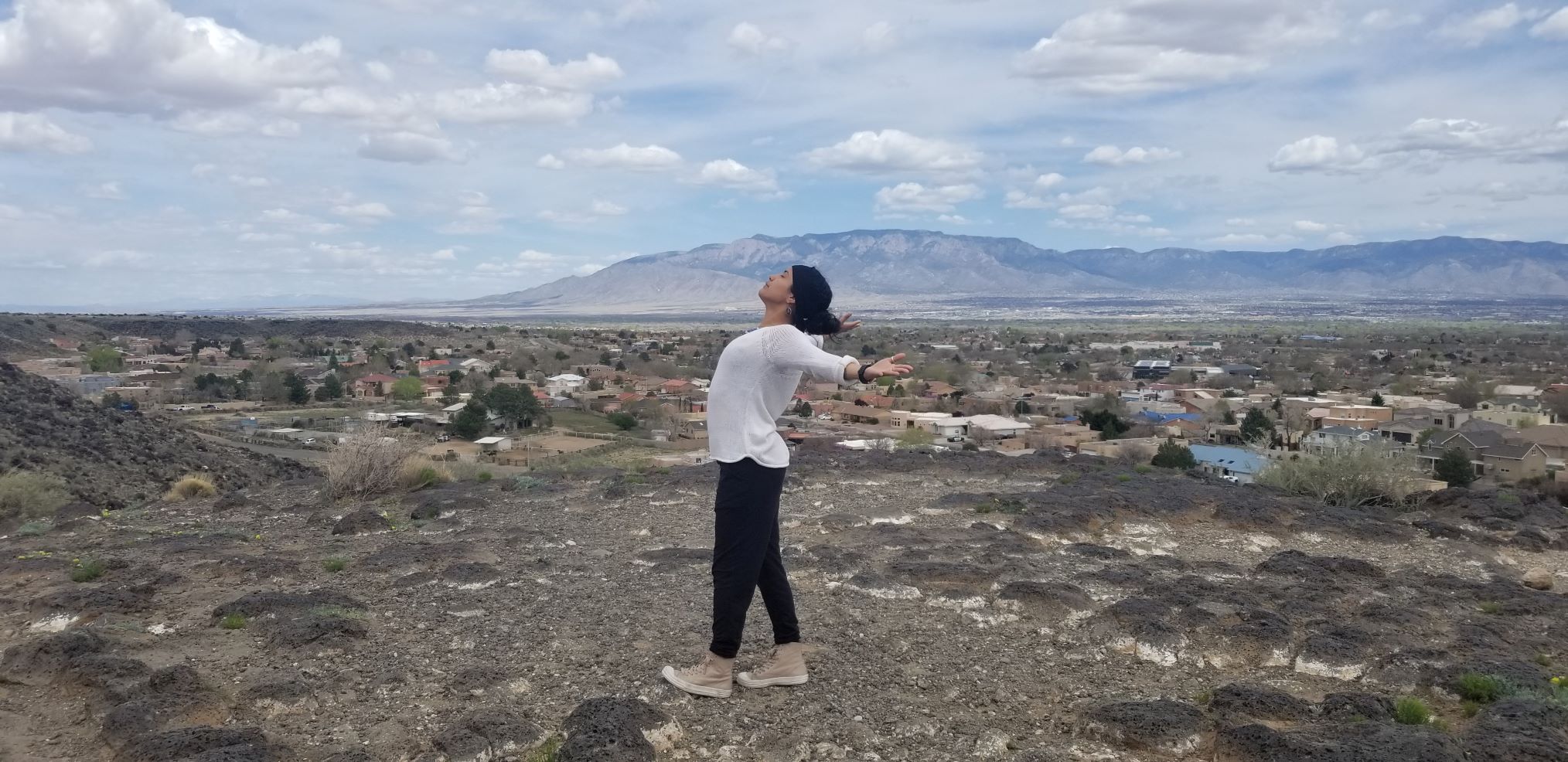 Woman stands on rocky terrain with her back arched and arms stretched out to the side
