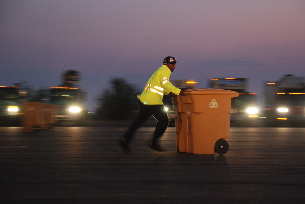 Man in yellow jacket pushing trashcan