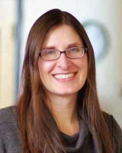 Woman with long straight brown hair and glasses smiles at the camera