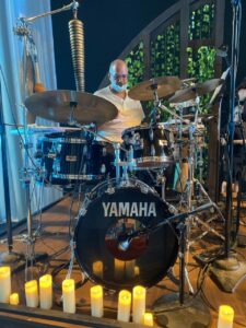A person sitting at a drum set with candles on the floor in front of them.