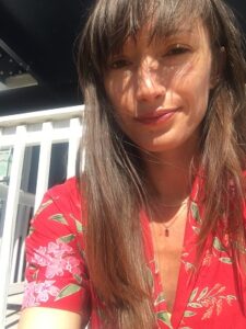 Woman with long straight hair wearing a red shirt looks at the camera.