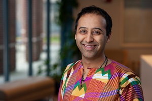 Individual with short dark hair, wearing a colorful sweater, is facing the camera, smiling. 