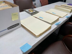 A row of manilla colored folders and a white box neatly laid out on a white table