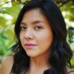 Natalie Benally, a dancer and choreographer from the Navajo Nation, stands beneath a green shade of trees. She carries a slight smirk on her face and stands determined in her stance. Photo: Morningstar Angeline.