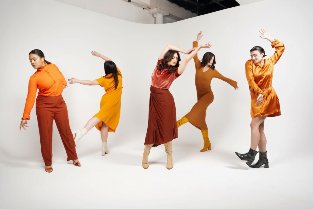 A professional photo of the Grounded Growth Marketing team shows five members, dancing in various shades of burnt or bright orange. Amy, the author of this article, is at the center with arms above her head, reaching off to the side.